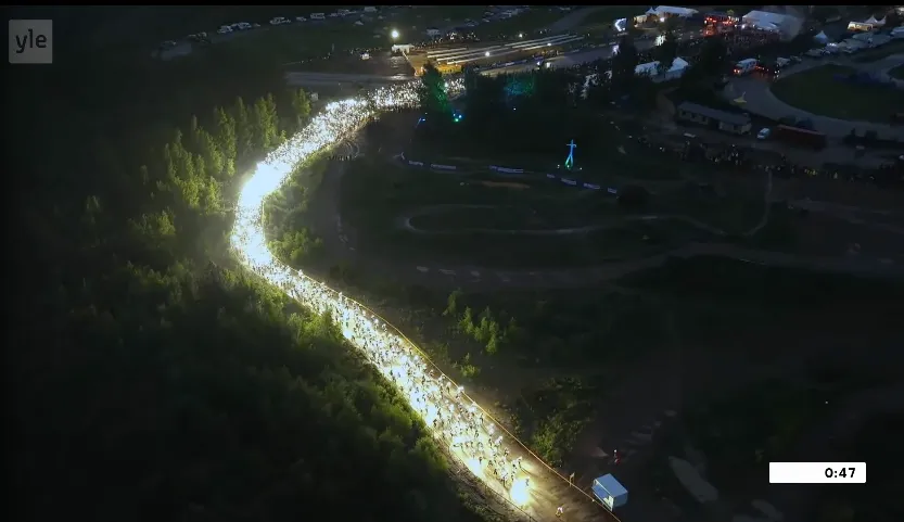 Hundreds of meters long line of light in the darkness of summer evening going through a path into the forest, shot from high above.